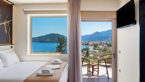A hotel room with a large window offering a view of a coastal town and mountains. - MANDRAGORAS ECO FRIENDLY (Perigiali)