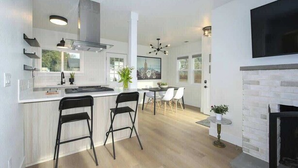 A modern kitchen with a central island, black bar stools, a dining area with a table and chairs, and a fireplace. - Downtown Camas Stay – Walkable, 15 Min to PDX (Camas)