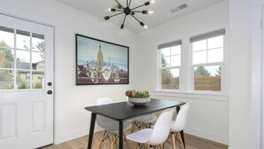 A dining area with a black table, white chairs, a cityscape painting, and a modern chandelier. - Downtown Camas Stay – Walkable, 15 Min to PDX (Camas)