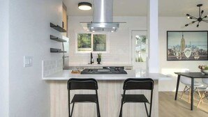A modern kitchen with a central island, two black chairs, a stainless steel range hood, and a dining area with a table and chairs. - Downtown Camas Stay – Walkable, 15 Min to PDX (Camas)