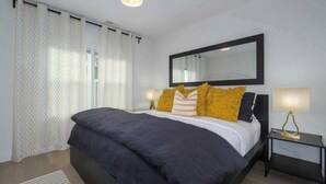 A bedroom with a bed, a nightstand, a mirror, and a window with curtains. - Downtown Camas Stay – Walkable, 15 Min to PDX (Camas)