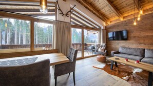 A spacious living area with a wooden ceiling, a large window overlooking a forest, a flat-screen TV mounted on the wall, and a cozy seating arrangement. - Chalet in Neukirchen Near Ski Lift (Neukirchen am Grossvenediger)