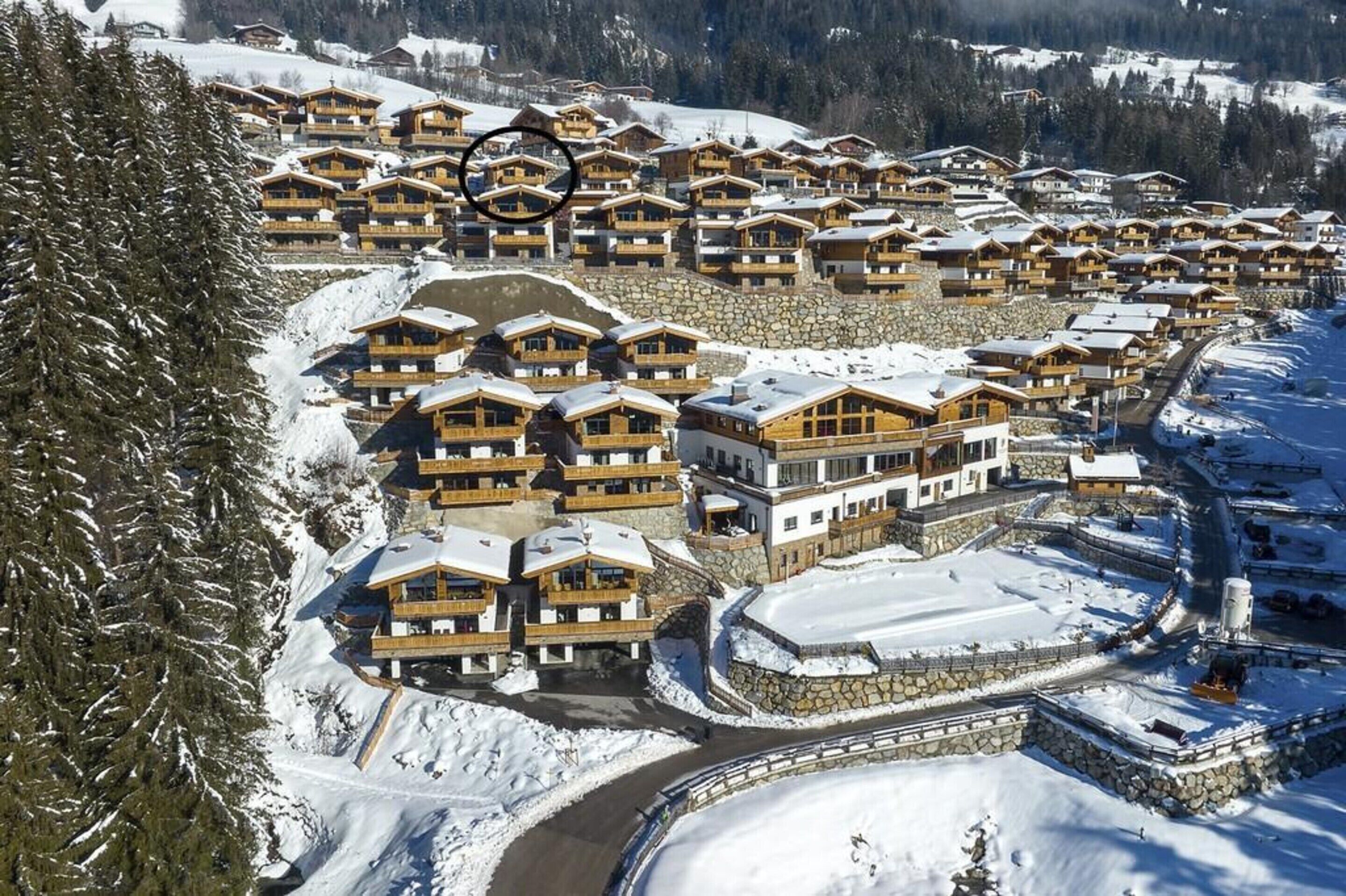 A snow-covered resort with multiple wooden buildings, a stone retaining wall, and a ski lift visible.