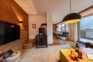 A modern living room with a fireplace, a TV, and a dining area with a view. - Chalet in Neukirchen Near Ski Arena Wildkogel (Neukirchen am Grossvenediger)