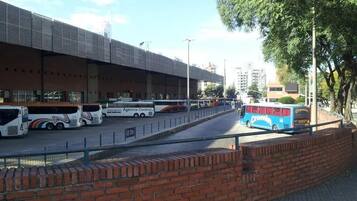 Una estación de autobuses con varios autobuses, un área de espera cubierta y un muro de ladrillo.