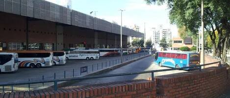 Una estación de autobuses con varios autobuses, un área de espera cubierta y un muro de ladrillo.