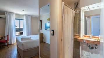 Ein Hotelzimmer mit Bett, Sessel, Badezimmer mit Dusche und Blick ins Freie.