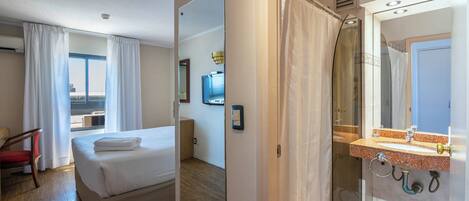 A hotel room with a bed, a chair, a bathroom with a shower, and a view of the outside.