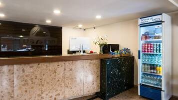 A reception area with a marble counter, a large poster, a refrigerator stocked with beverages, and a potted plant.