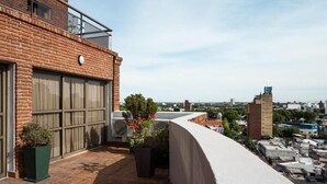 Una terraza en la azotea con un edificio de ladrillo, plantas en macetas y vistas de la ciudad.