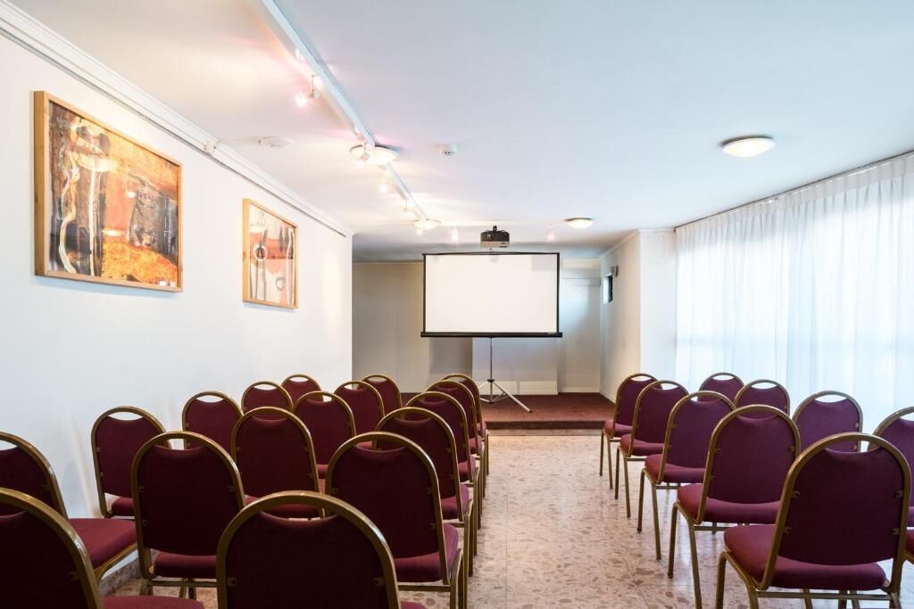 Ein Konferenzraum mit Reihen von Stühlen, einer Projektionsleinwand und Kunstwerken an den Wänden.