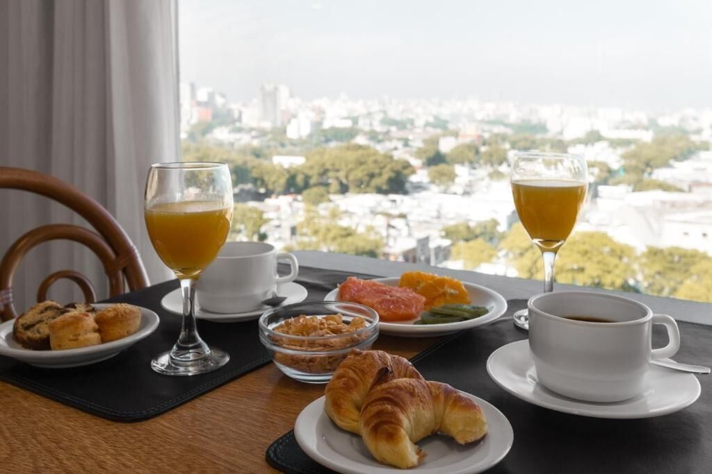 A breakfast setting with croissants, orange juice, coffee, and a view of a cityscape.