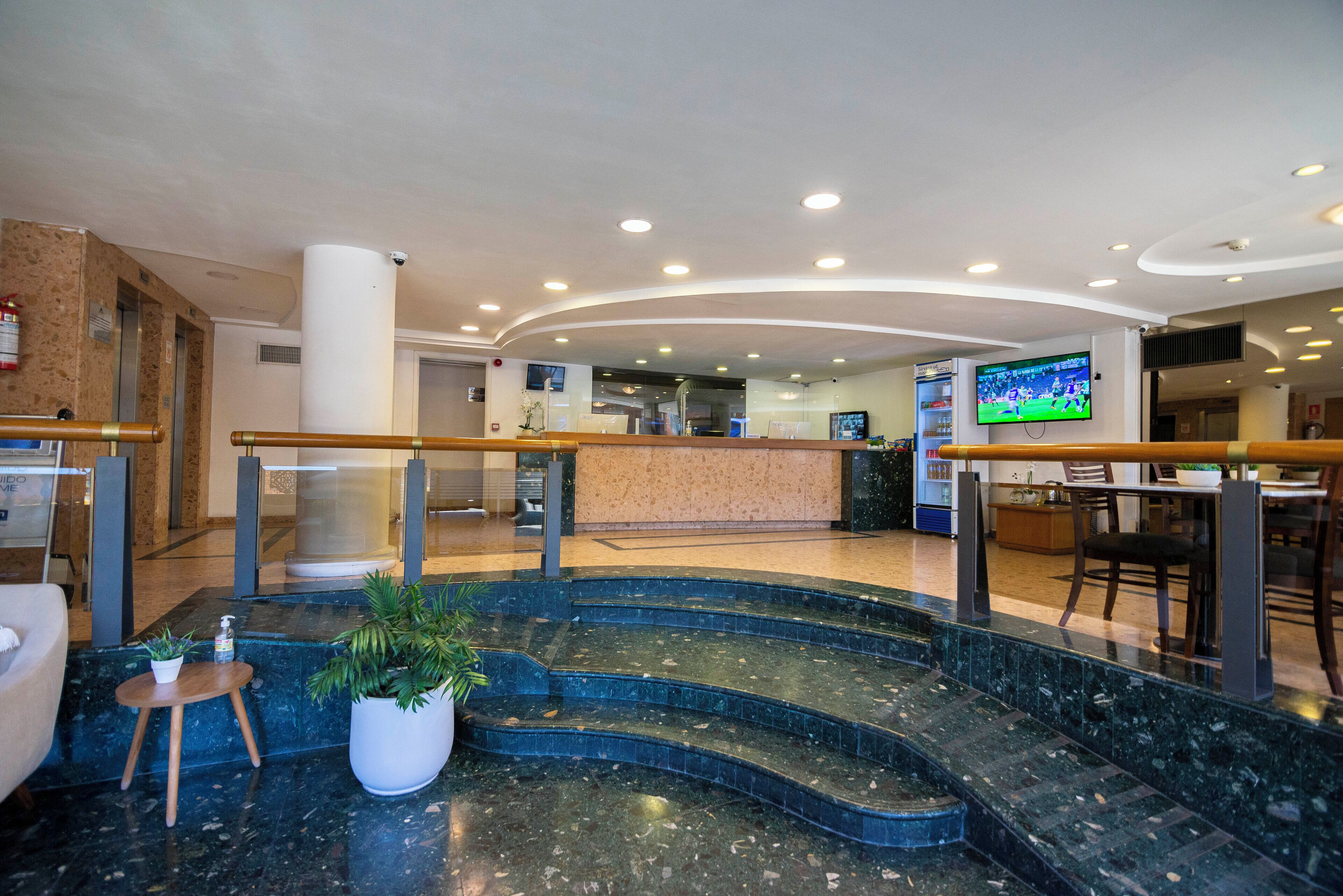 A hotel lobby with a reception desk, a staircase, and a television screen.