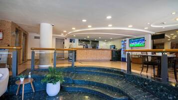 Un vestíbulo de hotel con un mostrador de recepción, una escalera y una pantalla de televisión.