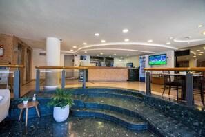 A hotel lobby with a reception desk, a staircase, and a television screen. - ALFA SUITES (Montevideo)