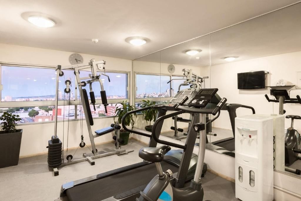 Un gimnasio con máquinas de cardio, pesas y un ventanal con vistas a la ciudad.