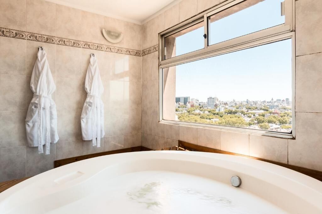 A modern bathroom with a large bathtub, two white towels hanging on the wall, and a city view through a large window.