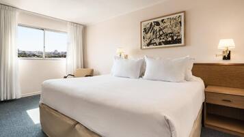 Quarto de hotel com uma cama grande, uma mesa de cabeceira, um abajur e um quadro na parede.