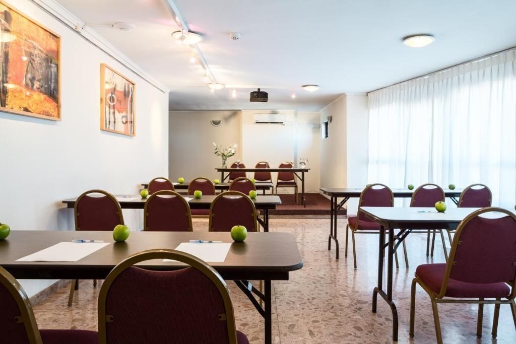 Uma sala de conferências com mesas e cadeiras, algumas delas com maçãs, e uma janela grande com cortinas.