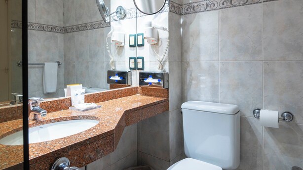 A modern bathroom with a granite countertop, a toilet, a bidet, and a large mirror. - ALFA SUITES (Montevideo)