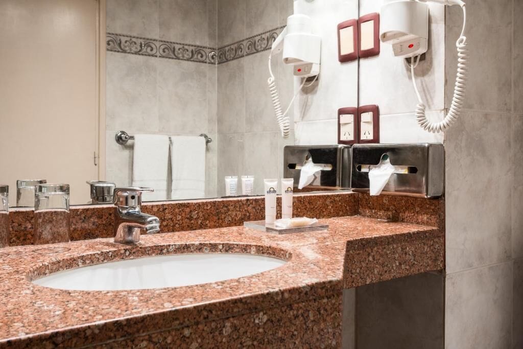 Une salle de bain avec un lavabo doté d’un plan de travail en granit, un miroir, un porte-serviettes et un sèche-cheveux.