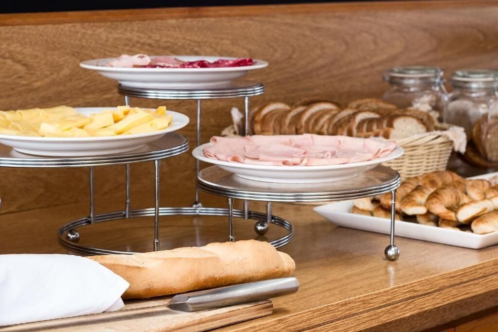 Una barra de buffet con platos de queso, jamón y pastelería sobre una mesa de madera.