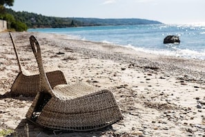 Two woven baskets on a pebbled beach with a view of the sea and distant hills. - Beachfront Villa in Chalkidiki - Greek Traditional Style (Moles Kalives)