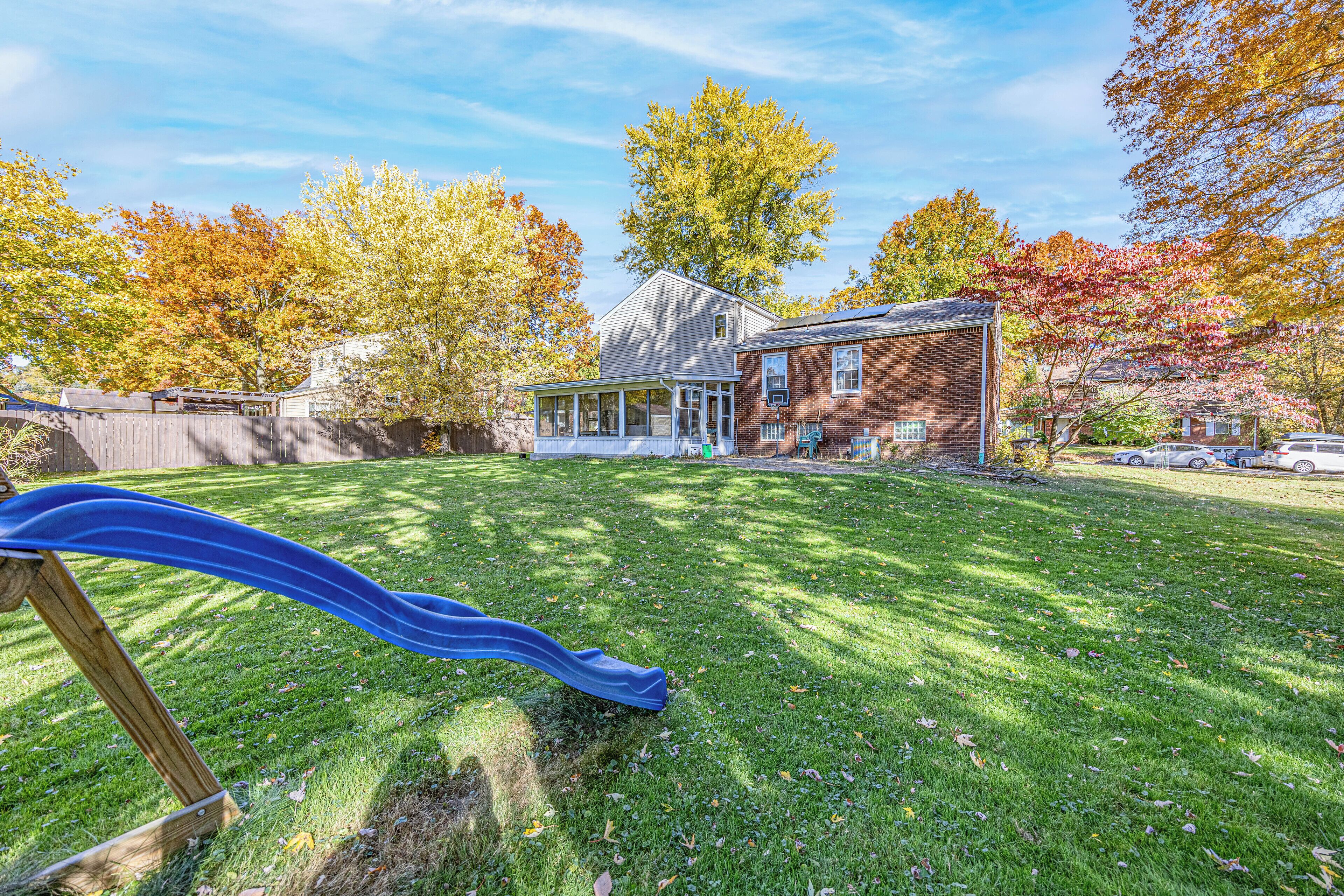 A backyard with a slide, a house, and autumn trees.