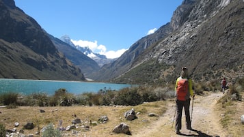 A hiker on a rocky trail with a lake and mountains in the background.