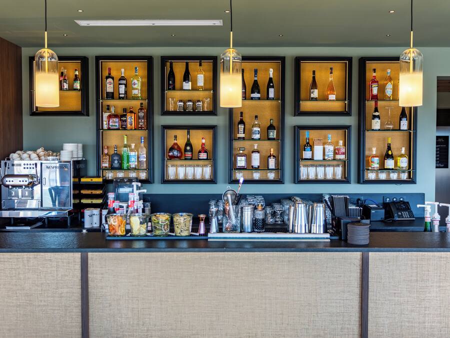 A bar area with shelves of liquor bottles, a coffee machine, and various bar tools.