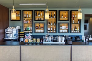 Zona de bar con estantes llenos de botellas de licor, una máquina de café y varios utensilios de bar.