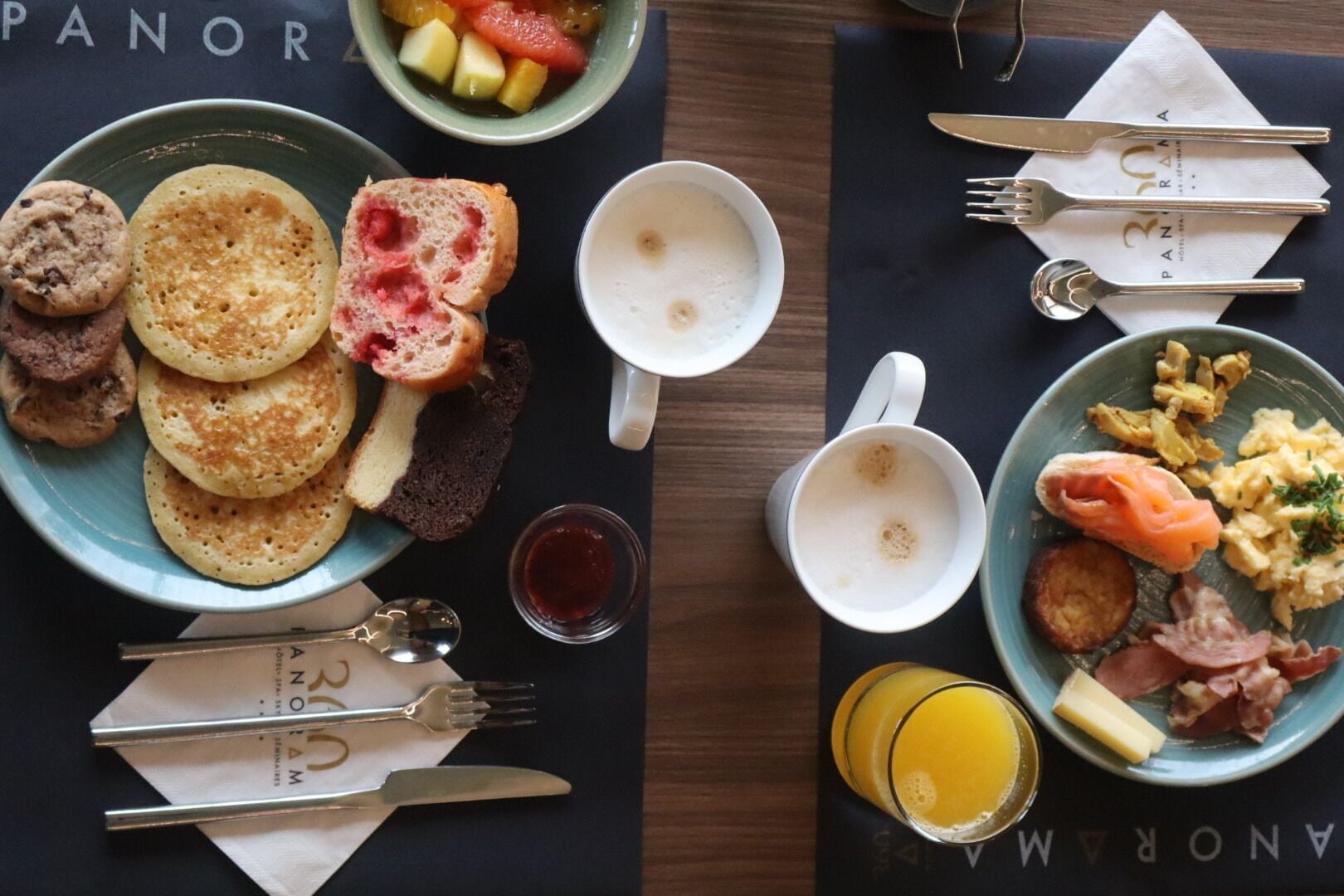 A breakfast setting with pancakes, toast, fruit, scrambled eggs, smoked salmon, and bacon.