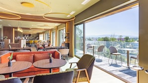 Un vestíbulo de hotel moderno con zona de comedor, una cocina al fondo y un balcón con mobiliario exterior.