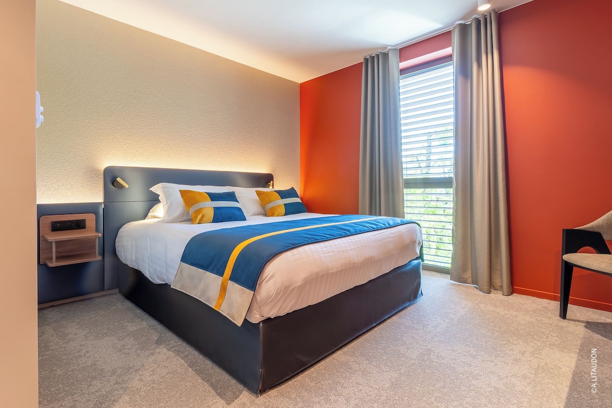 A modern hotel room with a large bed, a bedside table, and a window with curtains.
