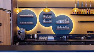 A modern bar area with a coffee machine, shelves with glassware, and hanging pendant lights.