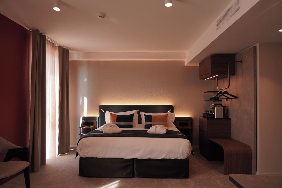 A modern hotel room with a large bed, bedside tables, a bench, and a wardrobe.