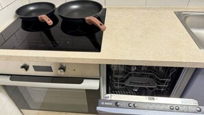 Eine Küche mit einem schwarzen Induktionskochfeld, zwei schwarzen Pfannen mit Holzgriffen, einem weißen Backofen und einem Bosch Geschirrspüler.