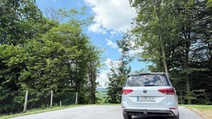 Ein silberner SUV steht auf einer asphaltierten Straße, flankiert von bewaldeten Hängen.