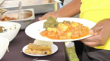 A person holding a plate with food, including a green dish and a red sauce with chunks, and a plate with rolled items and a slice of watermelon.