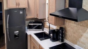 Cocina compacta con armarios de madera, un refrigerador negro, microondas, fregadero y estufa.
