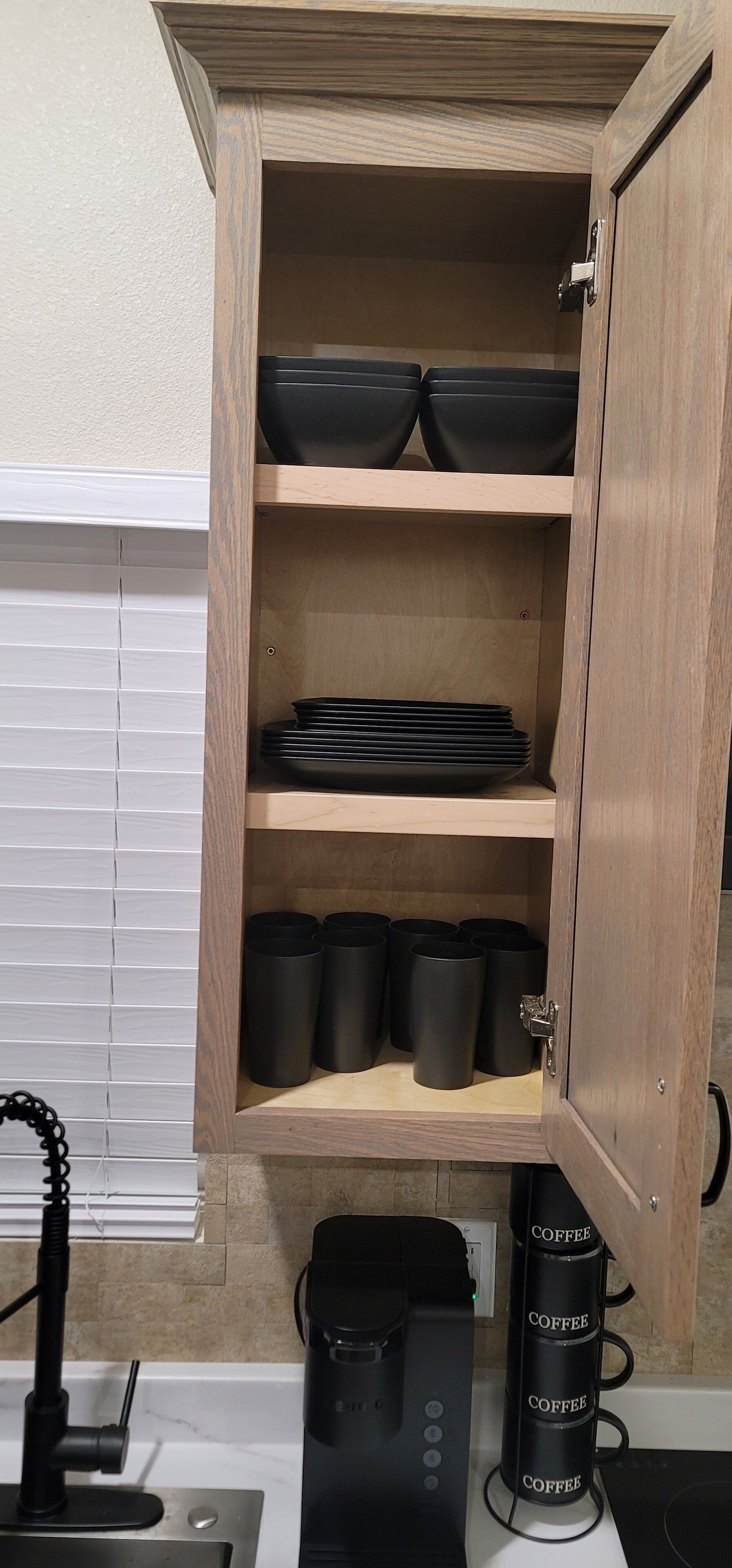 A wooden cabinet with shelves holding black bowls and cups.