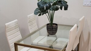Una mesa de comedor con cubierta de vidrio rodeada por cuatro sillas blancas con acolchado.