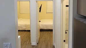 A hallway leading to a bedroom with two beds, wooden flooring, and a white door. - New Charming 2-bedroom Casita in nice El Centro with WiFi, AC (El Centro)