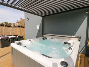 A hot tub with a wooden deck, a pergola overhead, and a wooden fence in the background.