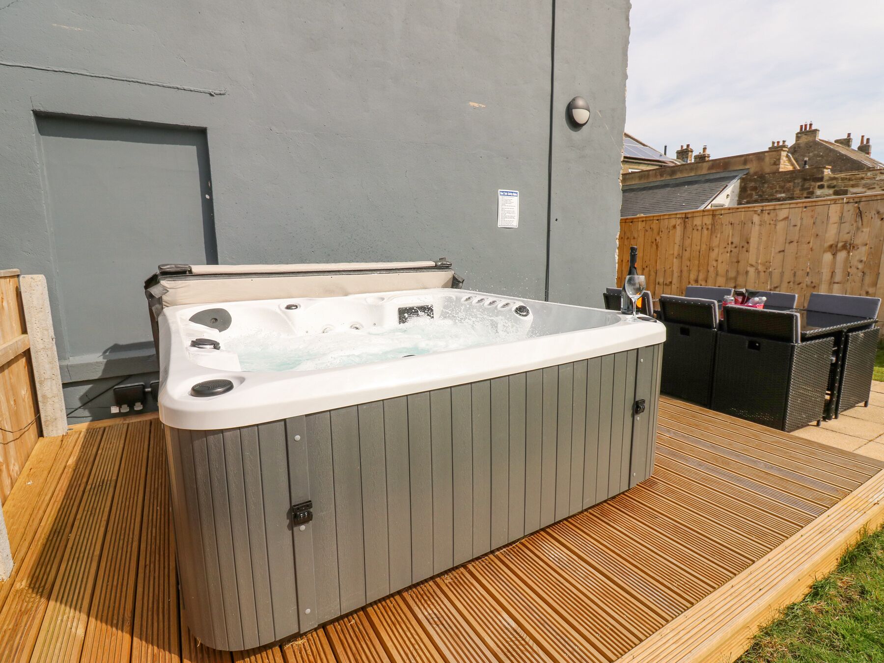 A hot tub on a wooden deck with a grey wall and a wooden fence in the background.