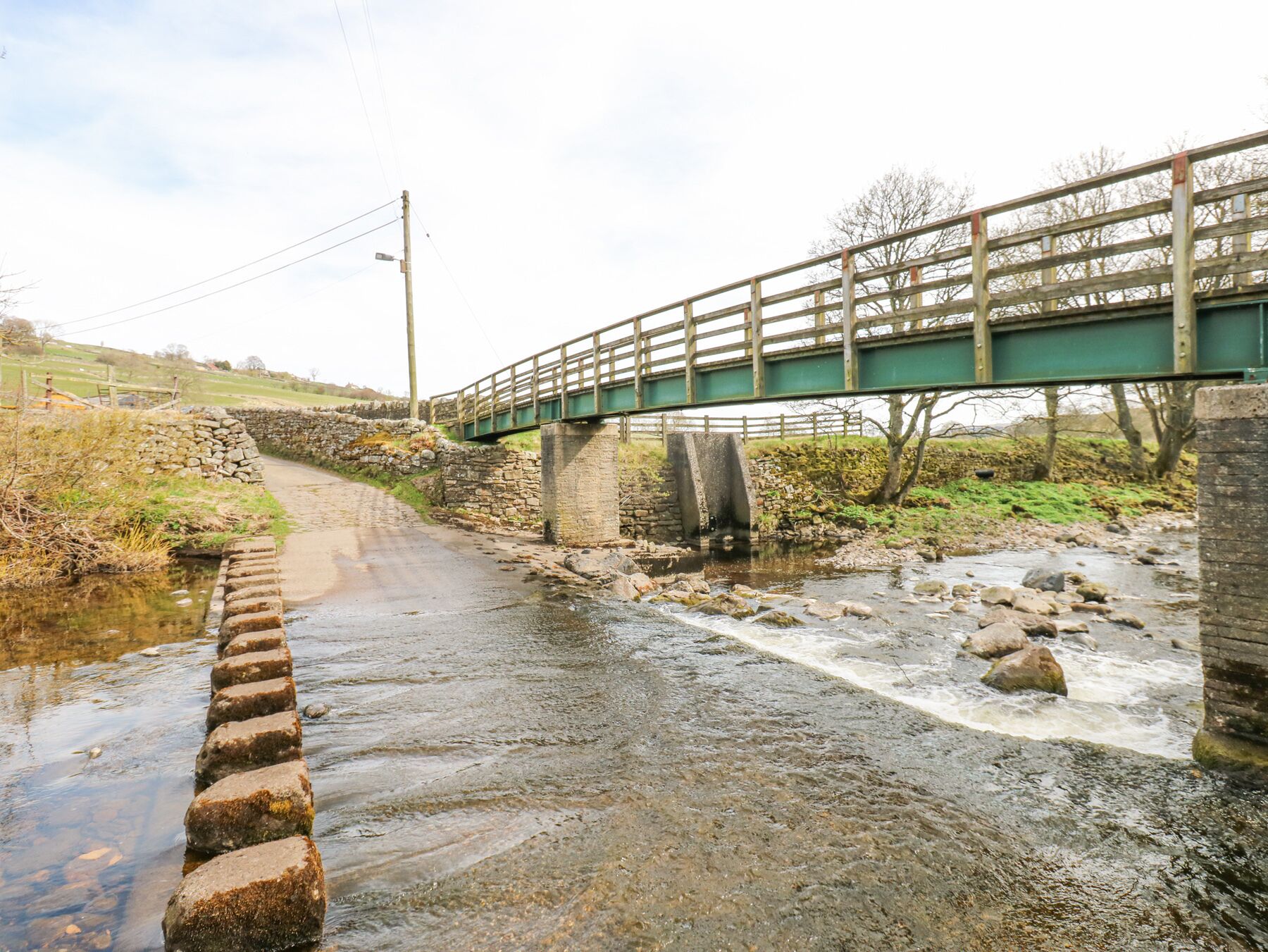 A stone bridge over a narrow stream with a wooden fence on top.
