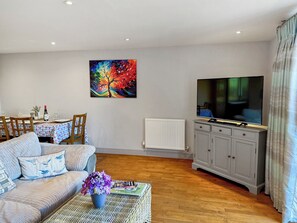 Ein Wohnzimmer mit einer Couch, einem Esstisch mit Stühlen, einem Fernseher, einer Heizung und einem Gemälde an der Wand.
