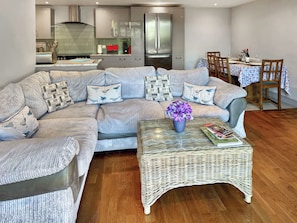 A modern living room with a sectional sofa, a glass coffee table with a vase, and a dining area with a table set for two.