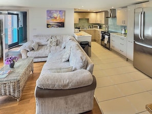 A modern living room with a sofa, a coffee table, and a kitchen area with a refrigerator and stove.