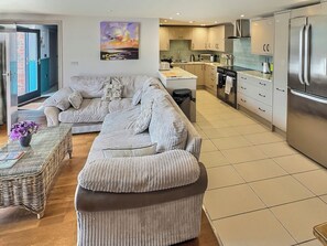A modern living room with a sofa, a coffee table, and a kitchen area with a refrigerator and stove.